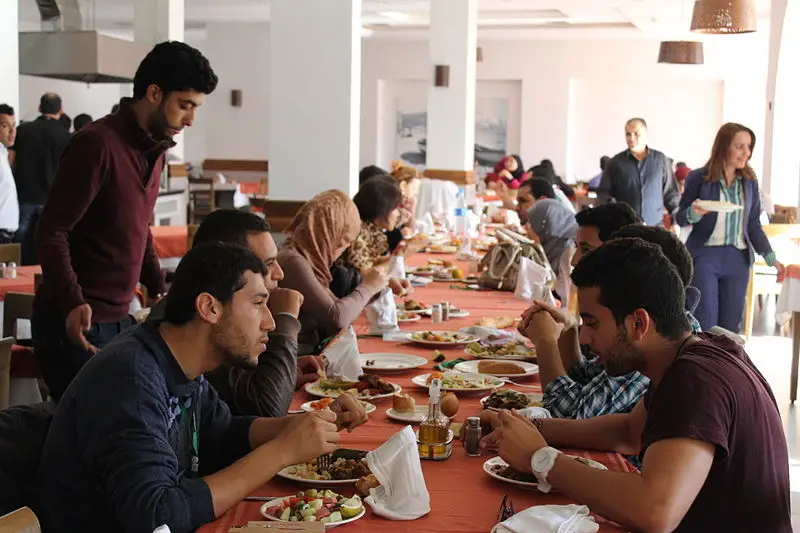 A picture of people eating together at a long rectangular table.