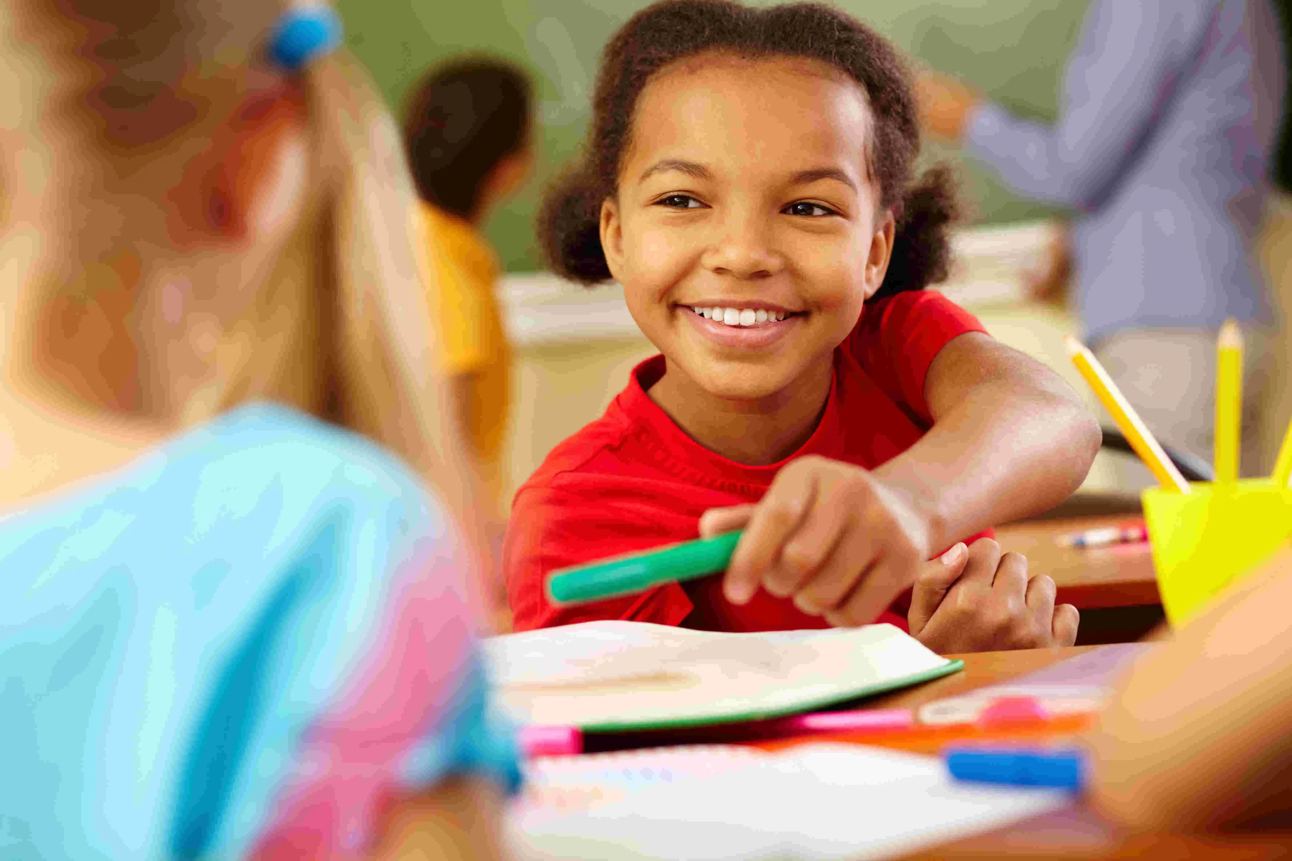 A picture of a little girl smilling while handling over a green pencil.
