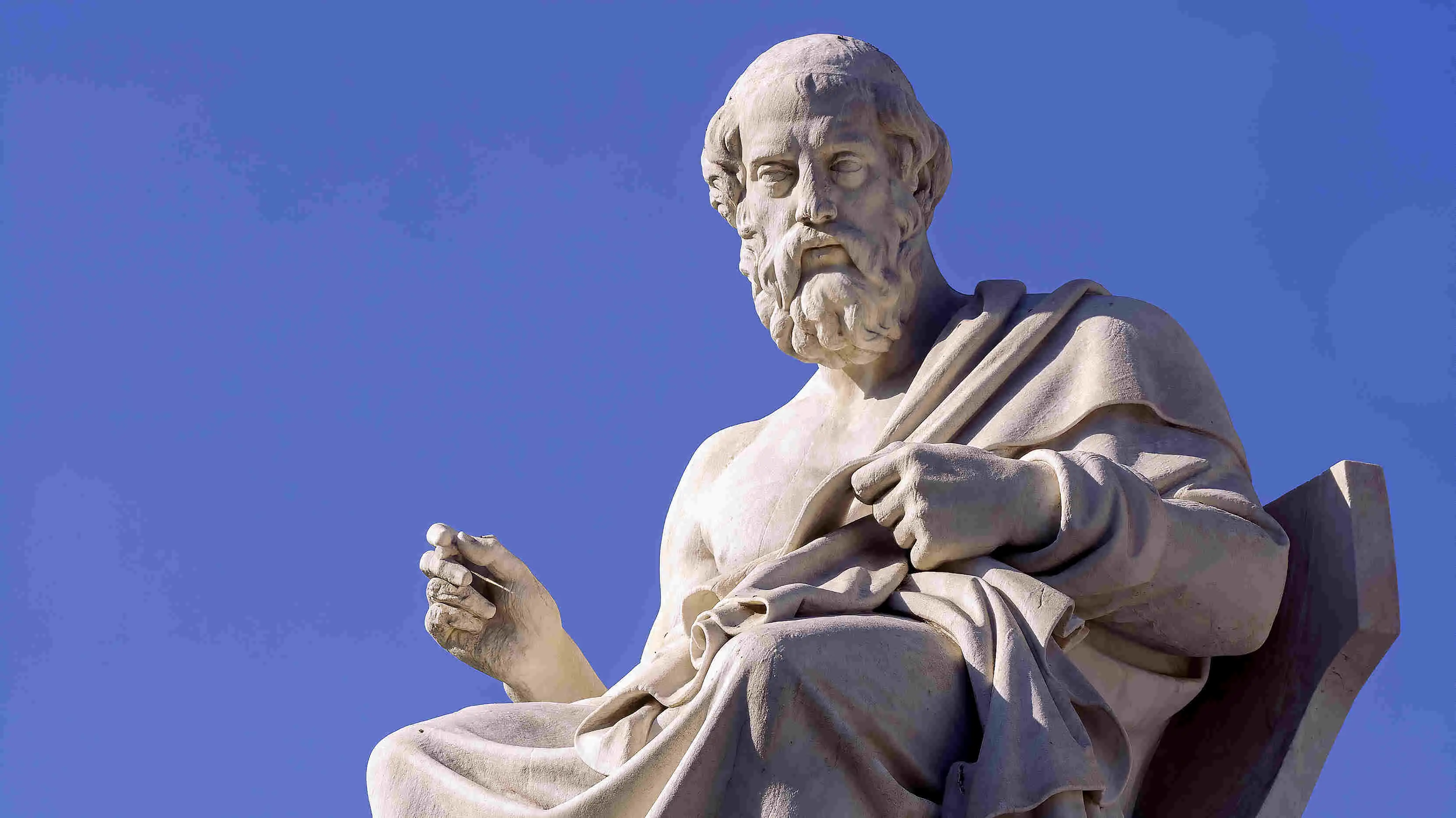A picture of a stone statue of Plato with a blue sky background.