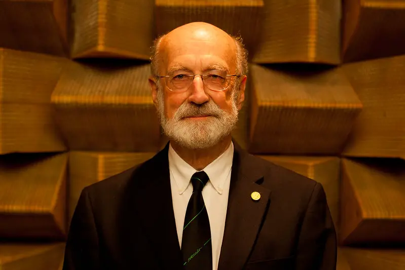 A picture of a older man with a suit, a tie and thin glasses looking directly at the camera.