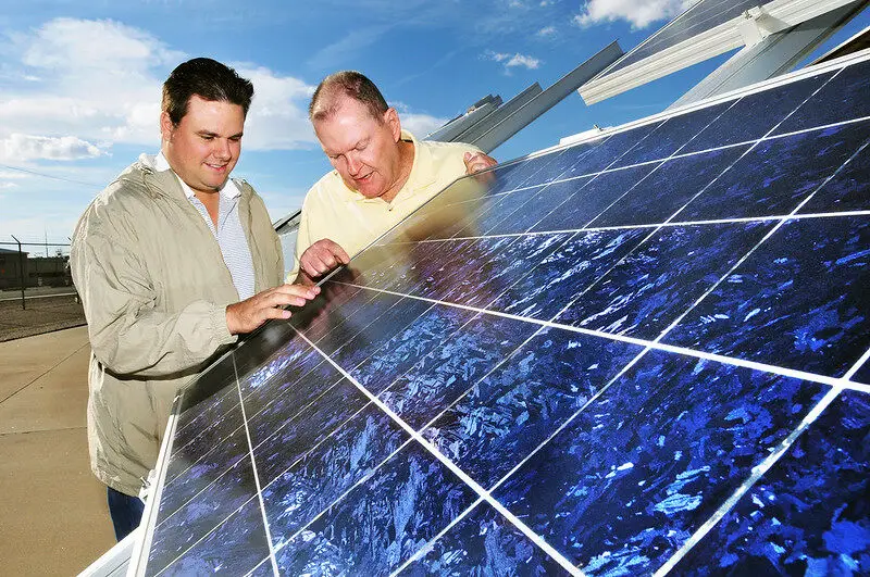 A picture of two men looking closely at a solar panel.