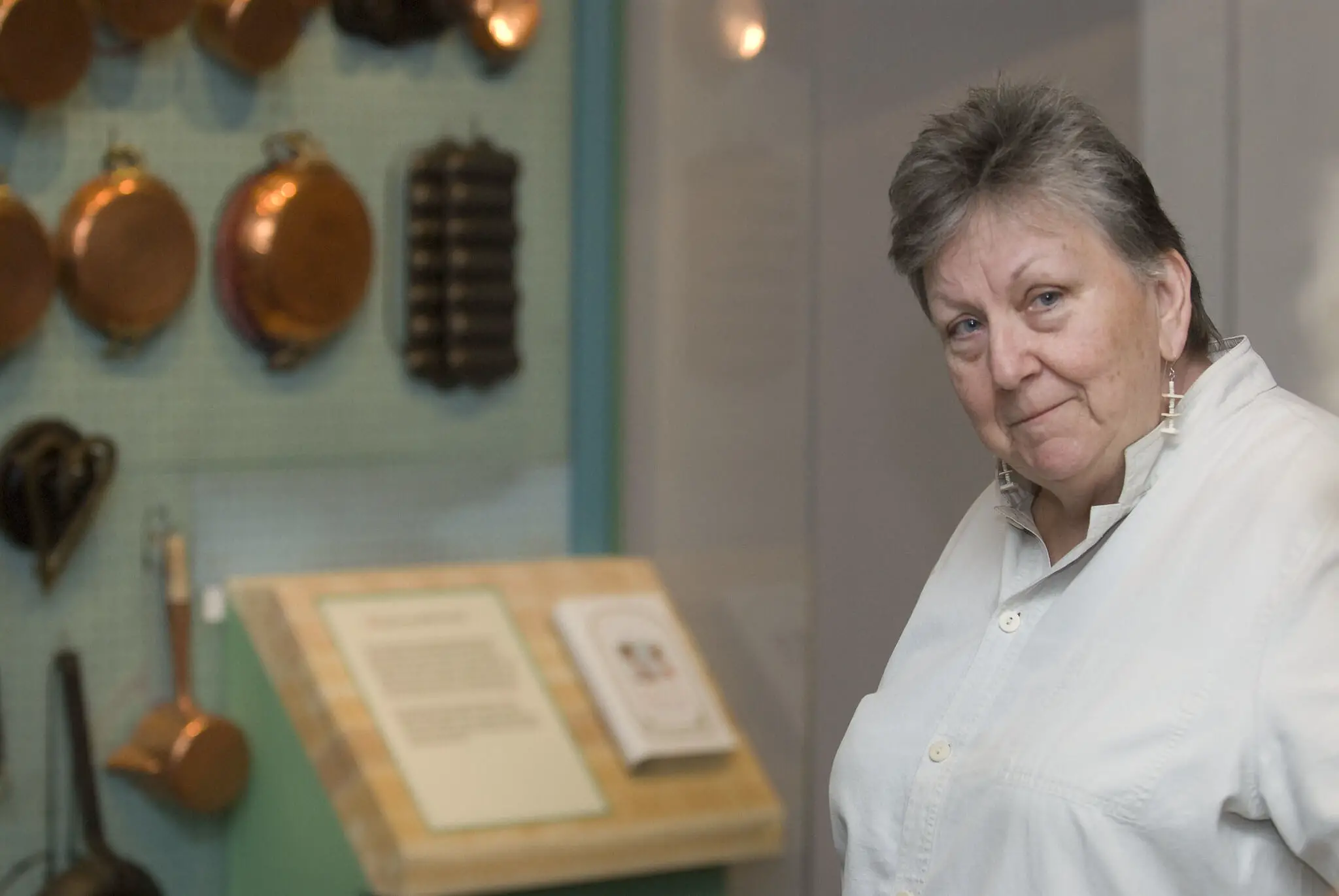 A photo of a older woman in white shirt in front of a exhibition.
